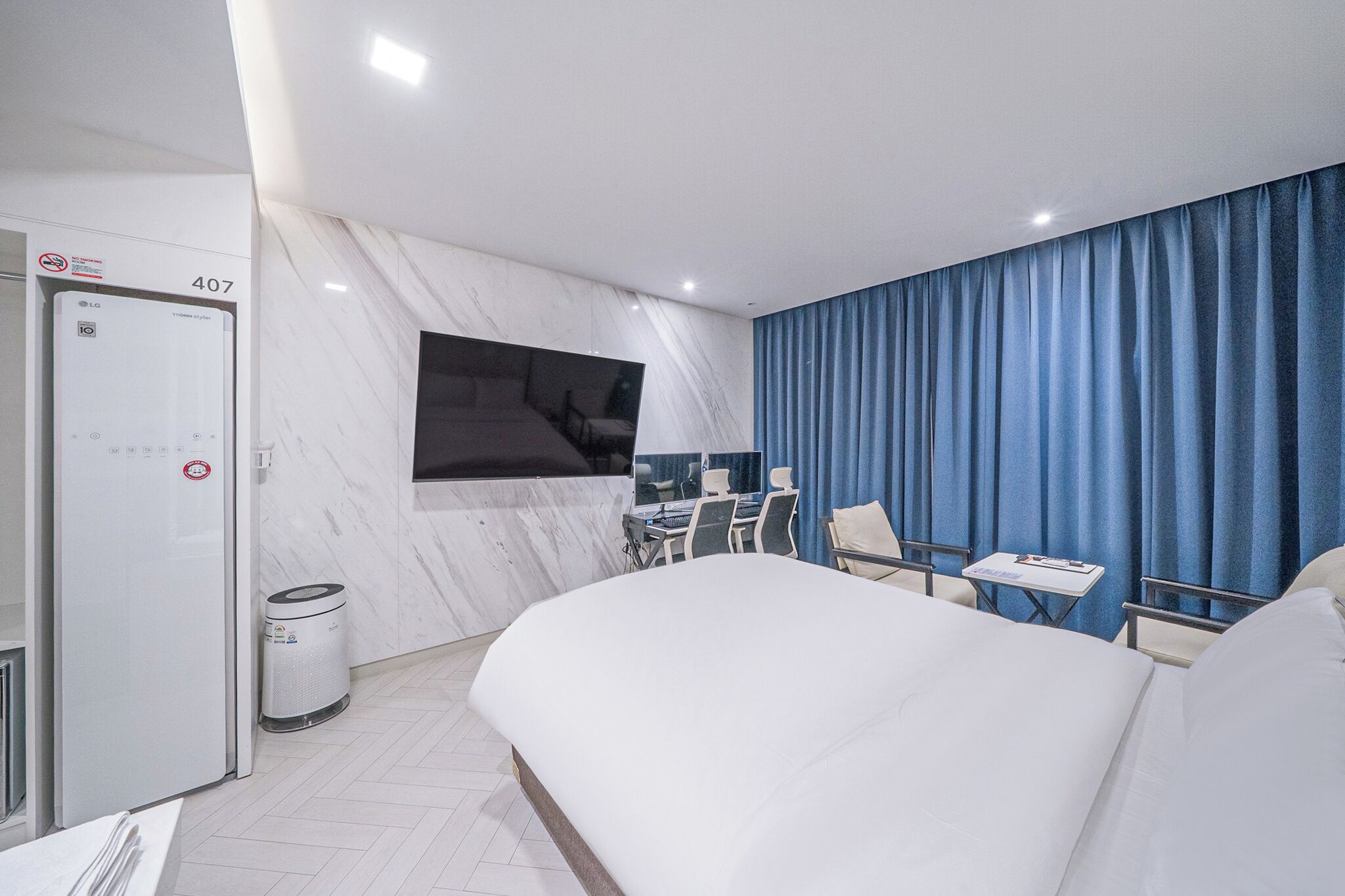 A hotel room with a bed, a desk with chairs, a TV, and a bathroom with a toilet and trash can.