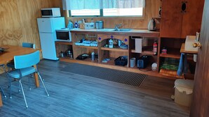 A compact kitchen with a microwave, toaster, and sink. There is a dining area with a table and chairs. - Stargazer's Cabin (Saint Arnaud)