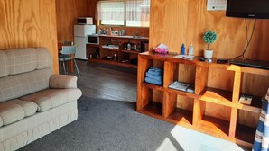 A cozy room with a sofa, a wooden desk with a laptop, a small kitchen area, and a calendar on the wall. - Stargazer's Cabin (Saint Arnaud)