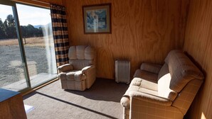 A cozy room with a large window, a radiator, and two sofas. - Stargazer's Cabin (Saint Arnaud)