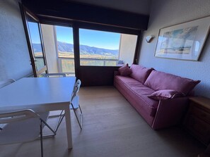 Een kamer met een witte tafel, een paarse bank en een groot raam met uitzicht op de bergen.