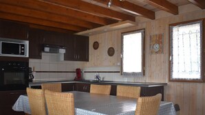 Eine Küche mit Holzausstattung, einer Mikrowelle, einem Backofen, einem Esstisch mit Korbstühlen und einem Fenster mit Vorhängen.