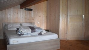 Ein Schlafzimmer mit Holzbalkendecke, einem Bett, einem Nachttisch und einer Tür.