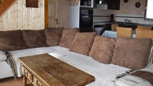 Ein gemütliches Wohnzimmer mit einem Ecksofa, einem Holztisch und einer Küchenzeile im Hintergrund.