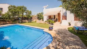 A swimming pool with a tiled deck, a covered outdoor seating area, and a small garden with potted plants. - Beach House Villa Isabel (Santanyí)