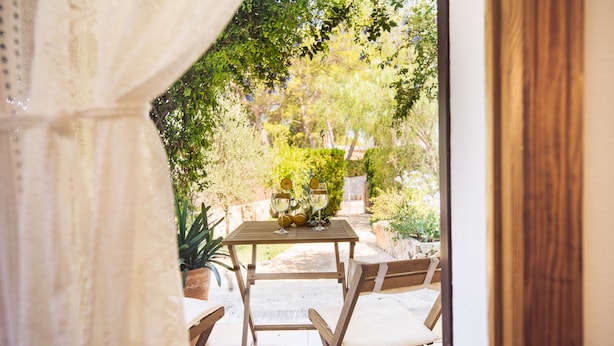 An outdoor patio with a wooden table and chairs, surrounded by greenery and plants. - Beach House Villa Isabel (Santanyí)