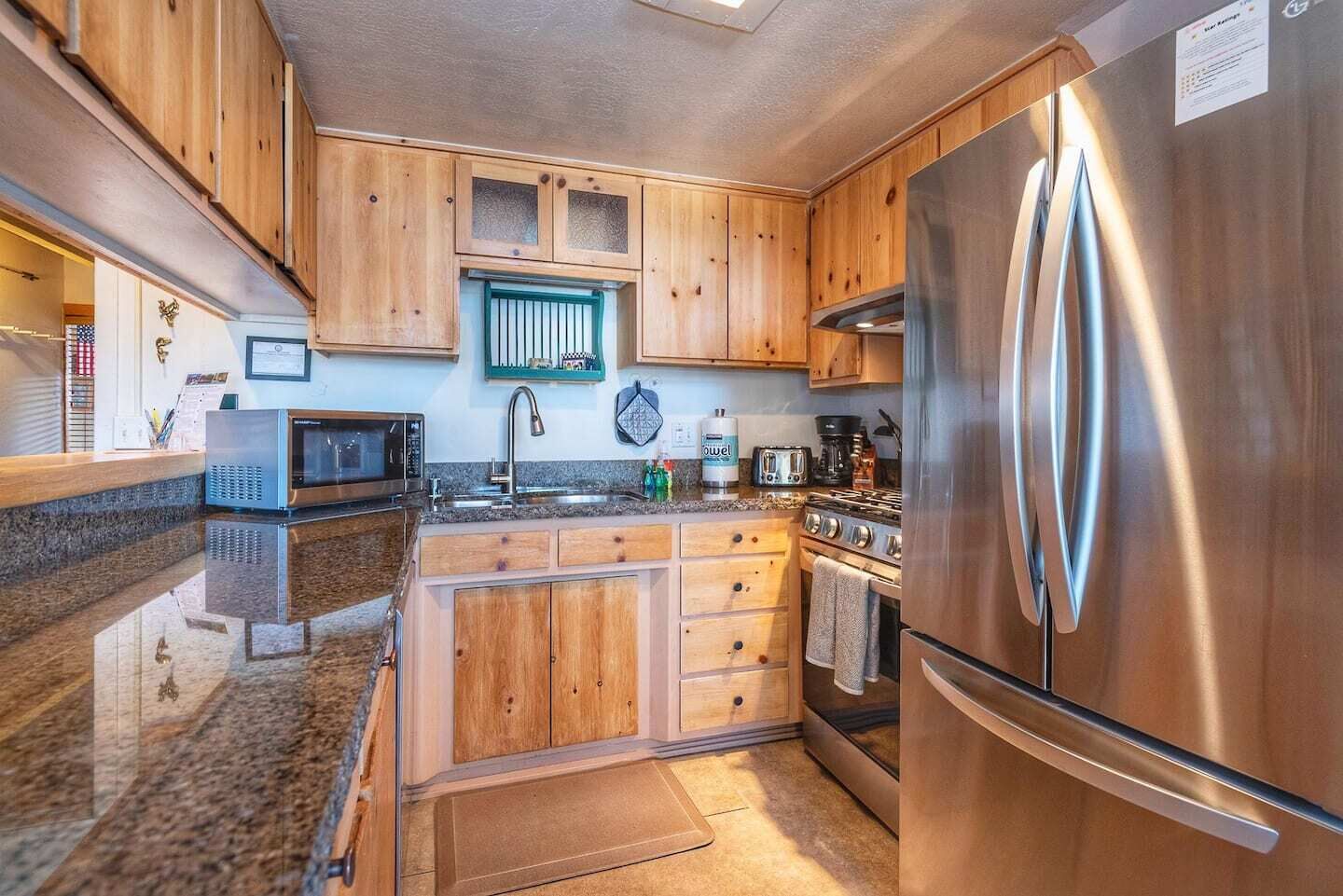 A kitchen with wooden cabinets, a stainless steel refrigerator, a microwave, a stove, and a sink.