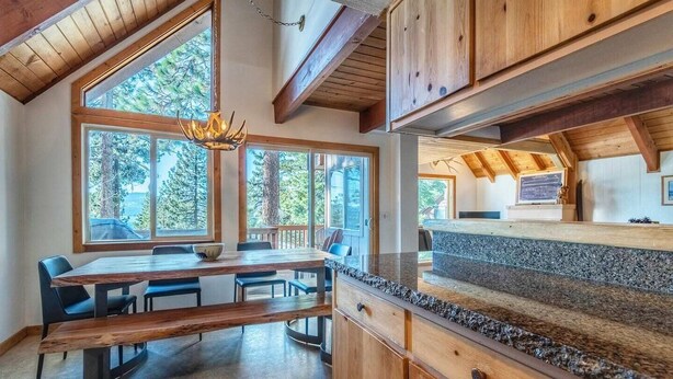 A modern kitchen with wooden cabinets, a granite countertop, and large windows offering a view of the outdoors. - Lakeview Serenity Cottage (Kings Beach)