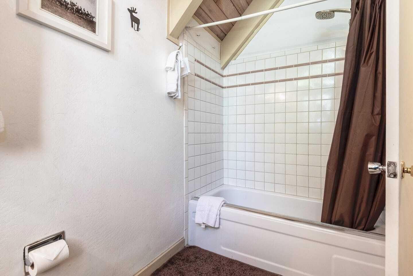 Une salle de bain avec des murs carrelés de carreaux blancs, une douche avec un rideau marron et un porte-serviettes avec des serviettes blanches.