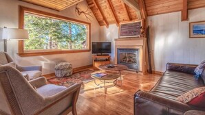 A cozy living room with wooden flooring, a fireplace, a television, and comfortable seating. - Lakeview Serenity Cottage (Kings Beach)