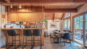 A wooden interior with a kitchen, bar area, dining table, and large windows. - Lakeview Serenity Cottage (Kings Beach)