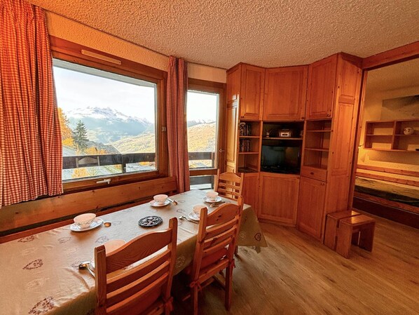 A cozy room with a wooden table set for two, a television, and wooden cabinets.