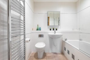 A bathroom with a toilet, sink, and bathtub, white tiles, and a mirror above the sink.
