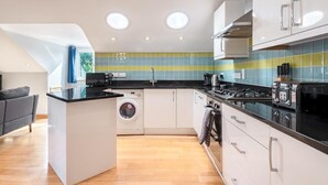 A modern kitchen with a central island, built-in appliances, and a washing machine. - Spacious Flat A Few Mins Walk to Carlyon Bay Beach (Carlyon Bay)
