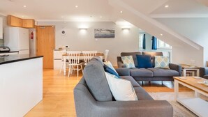 A modern living room with a grey sofa, a wooden dining table, and a kitchen area with white cabinets. - Spacious Flat A Few Mins Walk to Carlyon Bay Beach (Carlyon Bay)