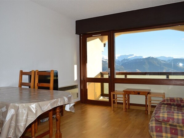 Um quarto com uma mesa de jantar de madeira e cadeiras, uma pequena mesa de madeira e vista para montanhas por uma grande janela.