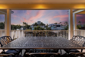 A covered outdoor dining area with a view of a large house and palm trees.