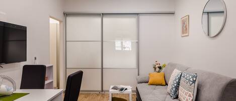 Una sala moderna con un sofá gris, una mesa de centro blanca, una silla negra, un televisor montado en la pared y un armario con puerta corrediza.