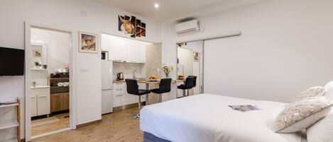 Un dormitorio moderno con una cama grande, un escritorio con dos sillas y una kitchenette.