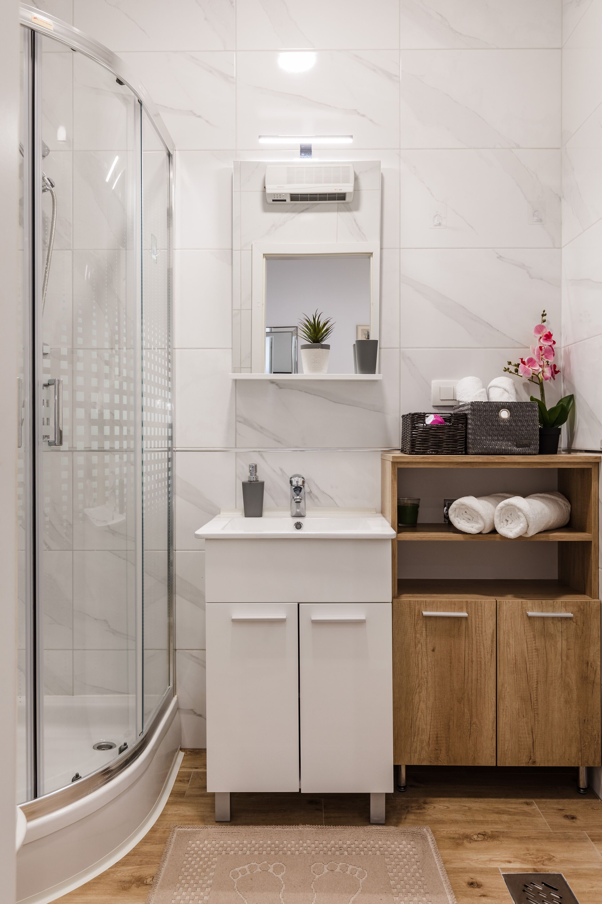 A modern bathroom with a glass-enclosed shower, a white vanity with a sink, and a wooden shelf with towels.