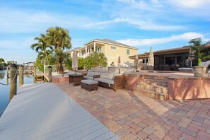 A waterfront property with a patio, outdoor furniture, and a pool area.