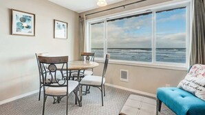 Een kamer met een groot raam met uitzicht op de oceaan, een eettafel met stoelen en een blauwe bank.