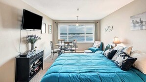 Een slaapkamer met een groot bed, een televisie, een eettafel met stoelen en uitzicht op zee.