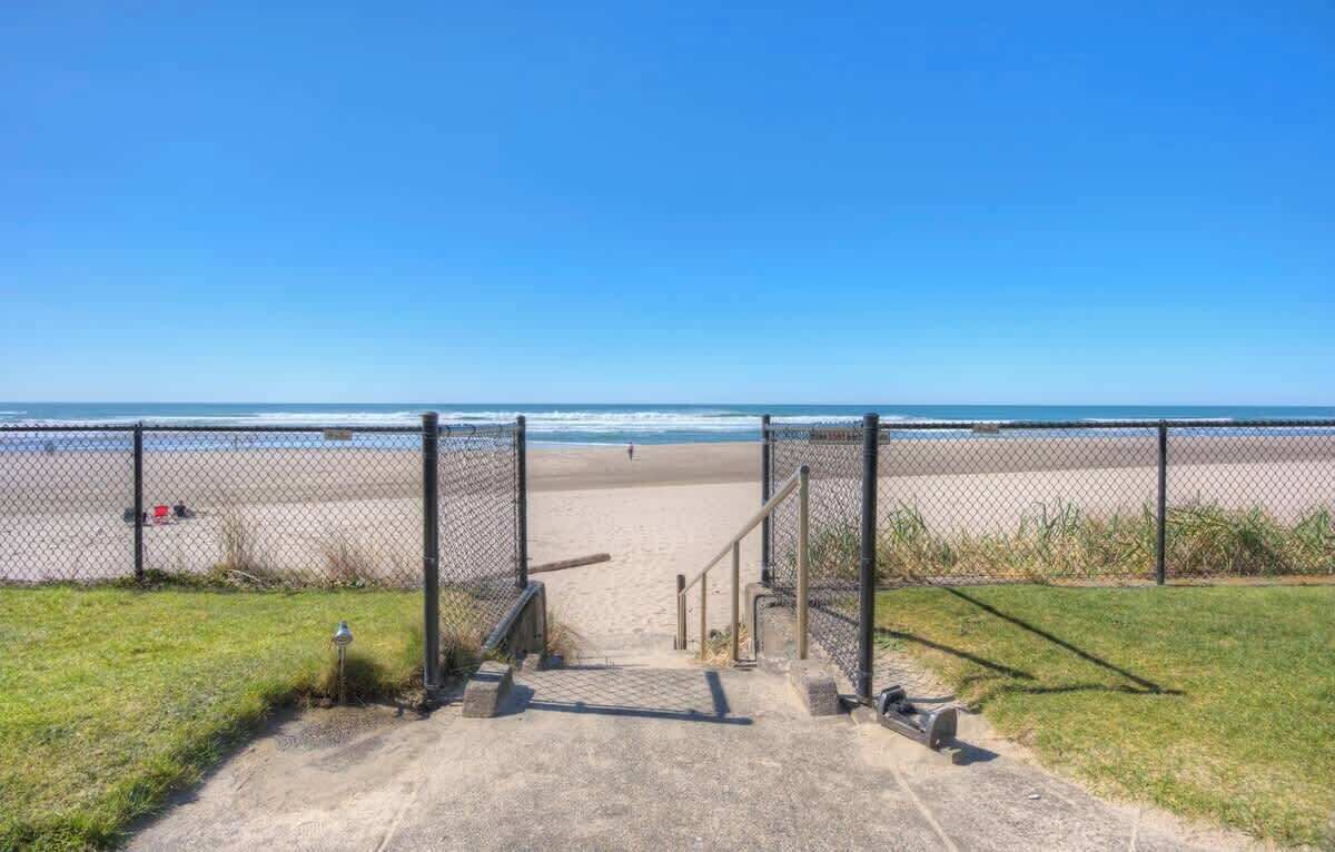 Uma trilha que leva a uma praia, com cerca e vista ampla do oceano.