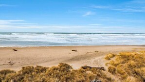 Een strand met zand en gras op de voorgrond, en de oceaan in de verte.