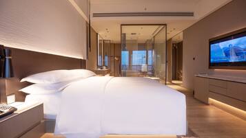 A modern hotel room with a large bed, a television, and a glass partition wall.