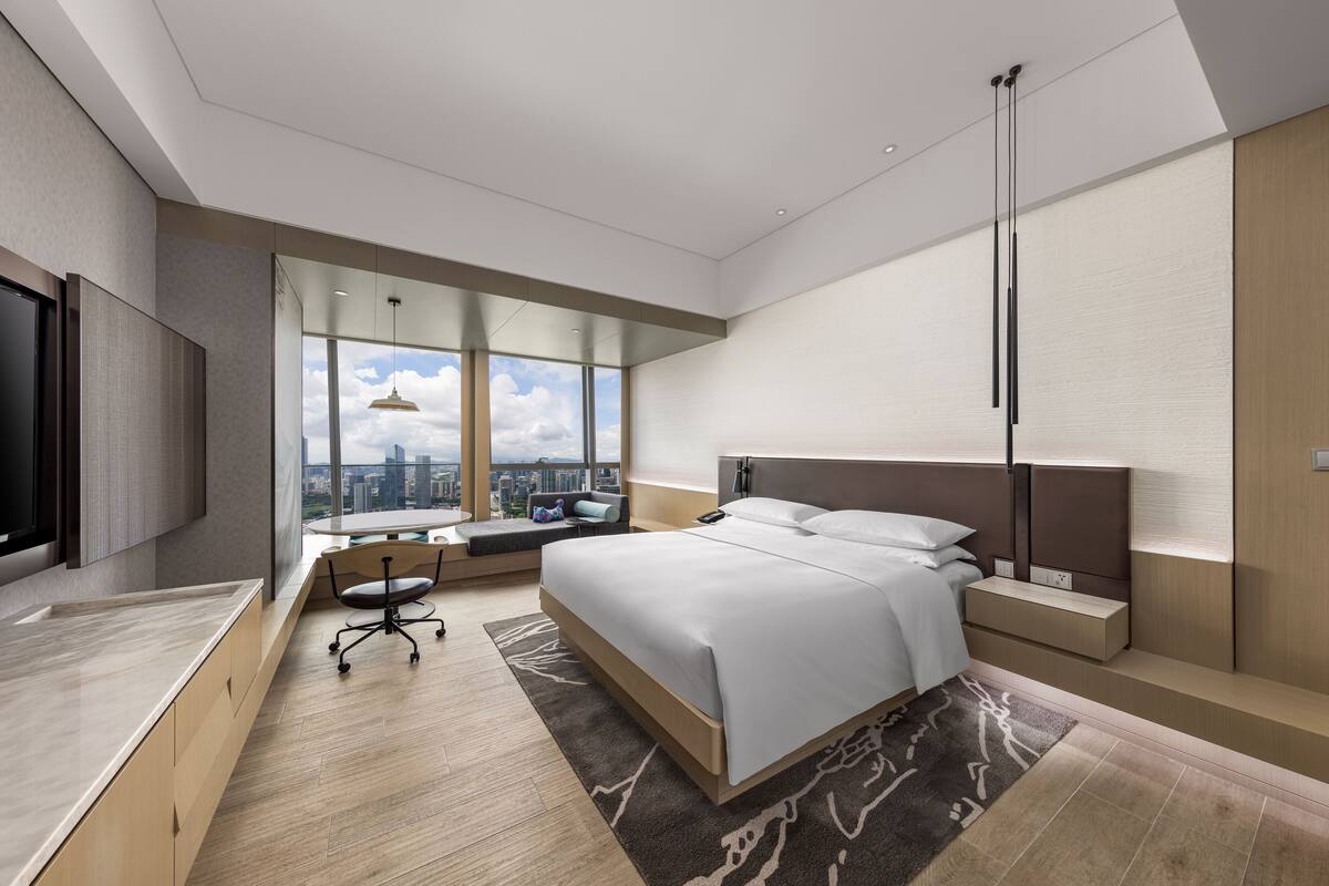 A modern hotel room with a large bed, a desk, and a view of the city.