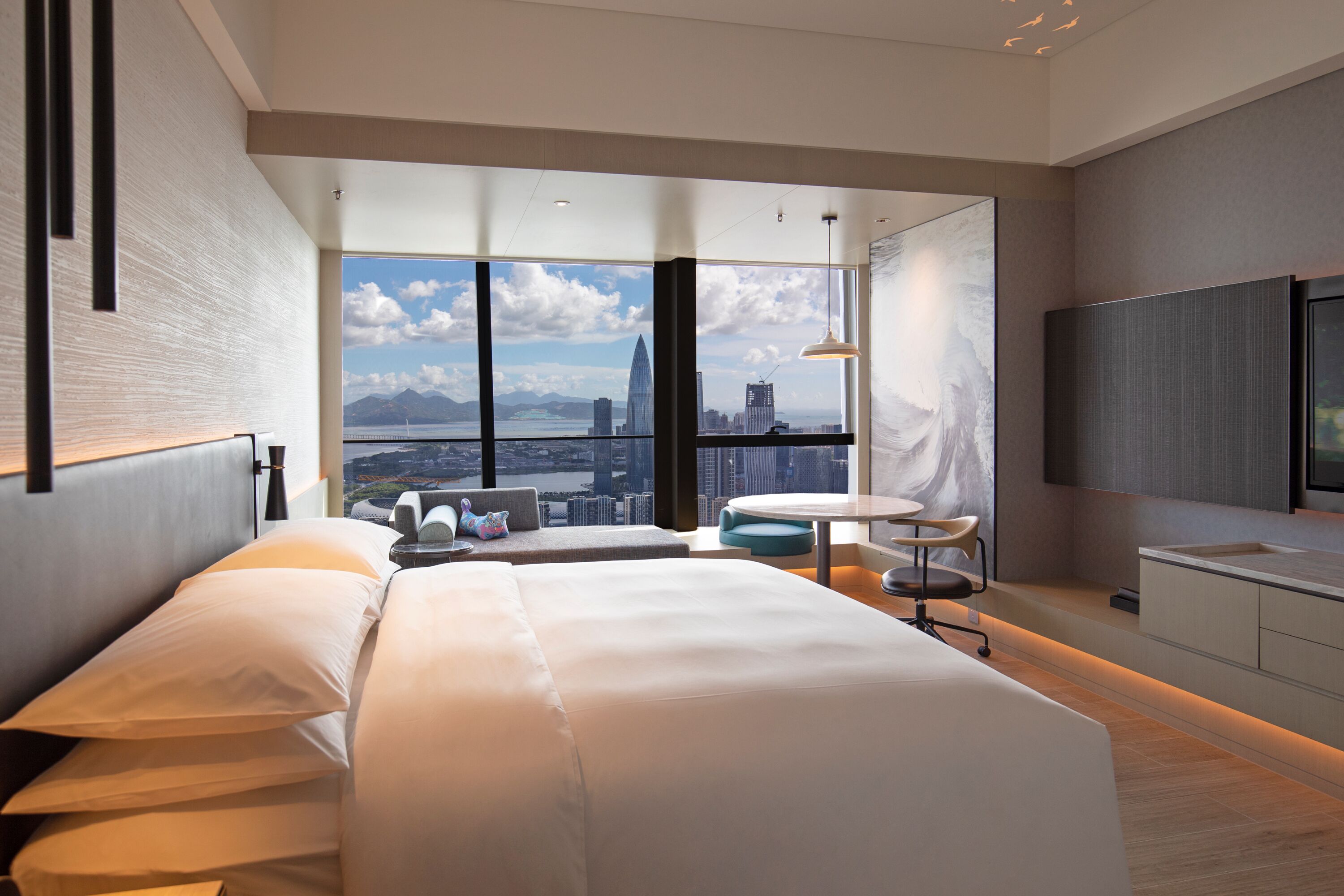 Une chambre d’hôtel moderne avec un grand lit, une petite table ronde et une vue sur le paysage urbain.