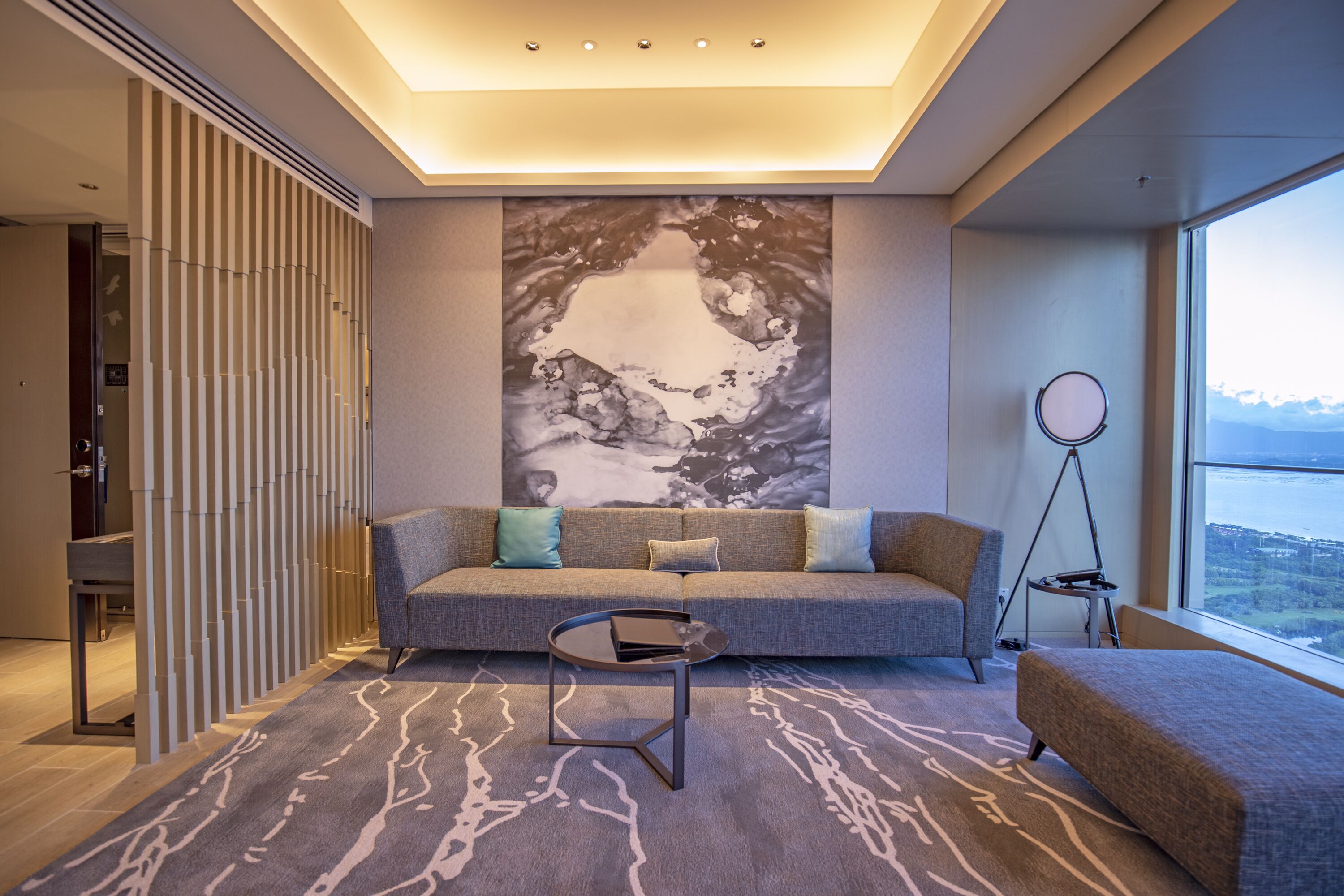 A modern living room with a gray sofa, a small round table, and a view of a mountainous landscape through a large window.