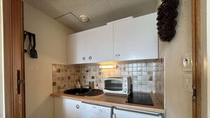A compact kitchen with a Bosch dishwasher, a white Bosch refrigerator, a white microwave, and a sink with a black mat.