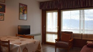 A living room with a dining table, a television, and a large window with a view of the mountains. - 2-Room Cabin Apartment with Parking in Font-Romeu (Font-Romeu-Odeillo-Via)