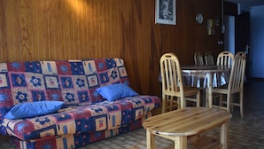 Una habitación acogedora con una pared de madera, un sofá estampado, una mesa de comedor de madera y sillas.