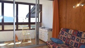 Una habitación con piso de madera, un sofá estampado, un armario de madera y una ventana con vista a las montañas.