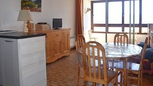 Un comedor con una mesa redonda y sillas, un aparador de madera, un televisor y una ventana con cortinas.