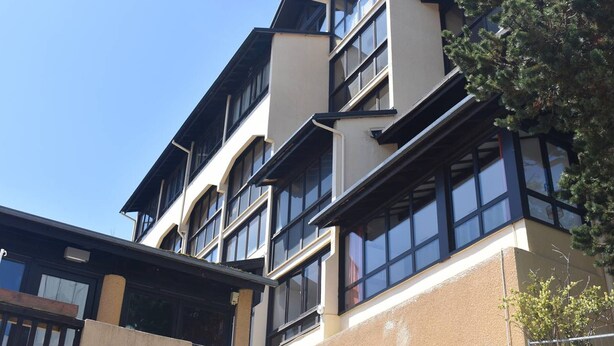 Un edificio de varios pisos con un diseño arquitectónico moderno, que presenta grandes ventanales y una combinación de paredes exteriores beige y de color oscuro.