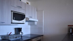 Una cocina con armarios blancos, microondas, cafetera y lavavajillas.