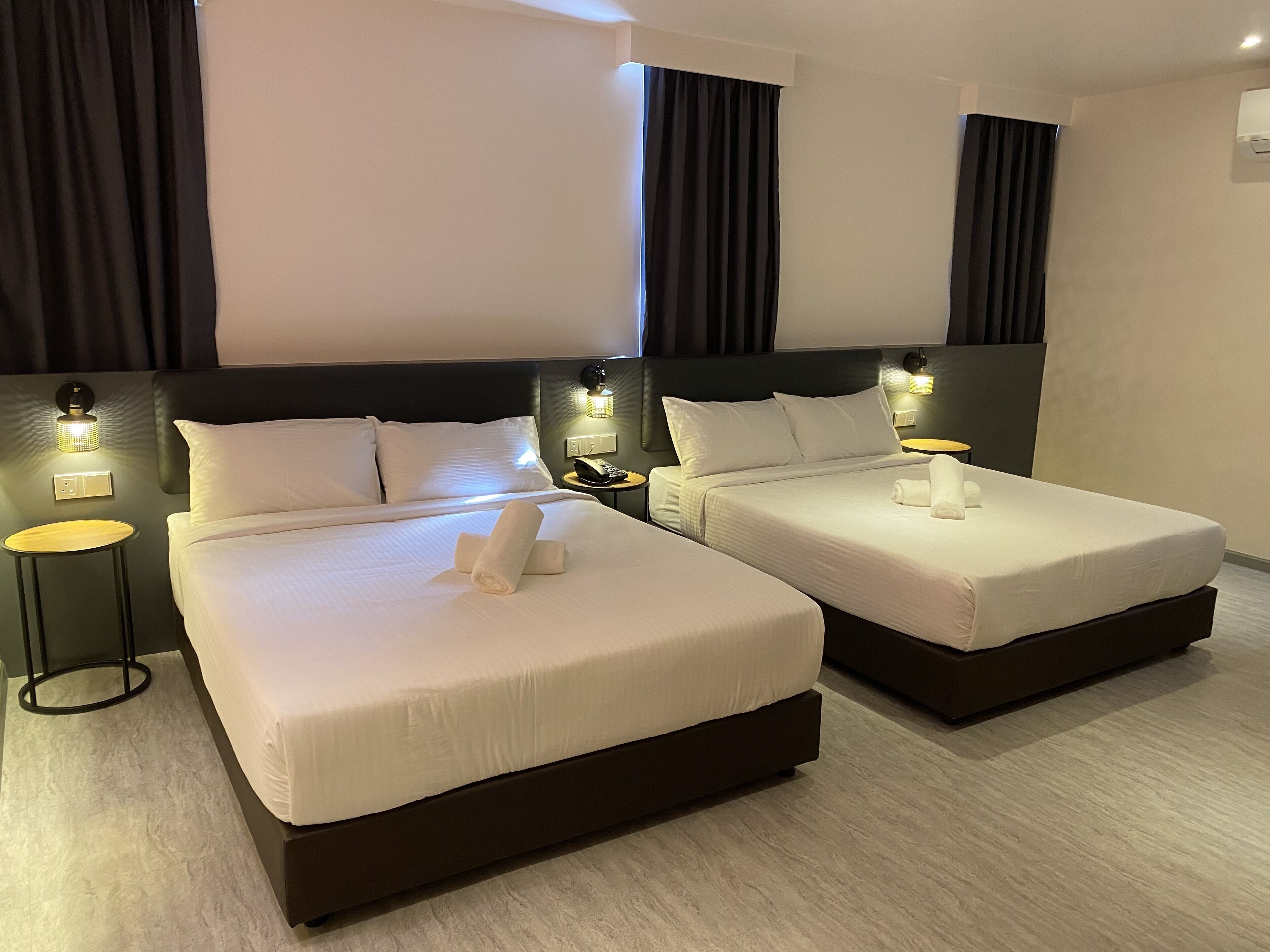 Two double beds with white linens, bedside tables with lamps, and a dark headboard.