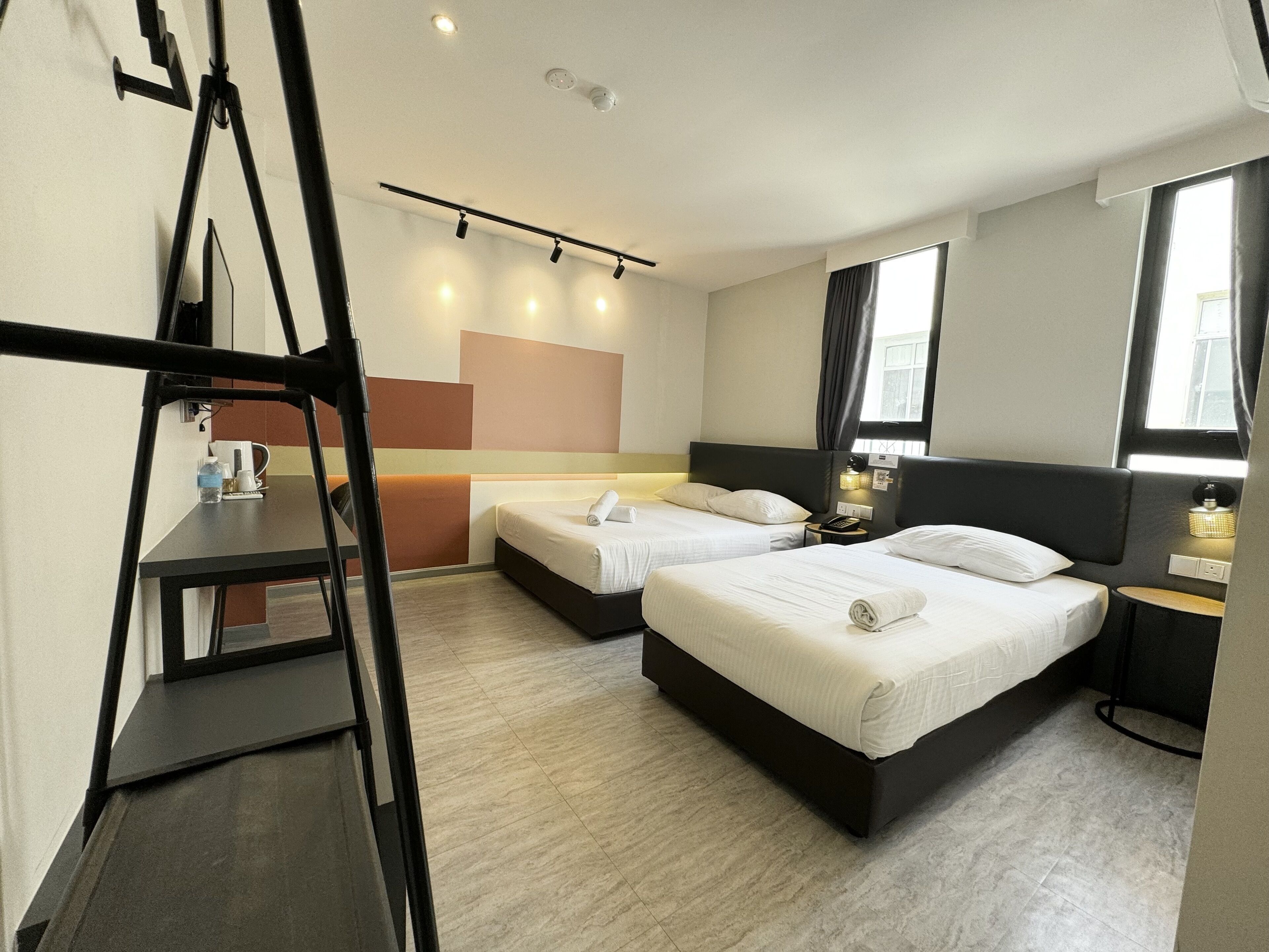 Une chambre d’hôtel avec deux lits, un bureau, une chaise, une fenêtre et un luminaire au plafond.