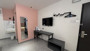 Una habitación de hotel moderna con un espejo grande, un televisor de pantalla plana montado en la pared, un escritorio con una silla y una estantería pequeña.