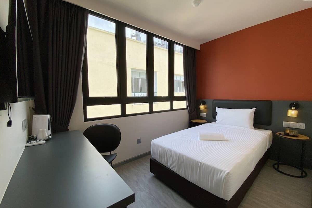 Habitación de hotel con cama, escritorio, silla, mesita de noche y ventana con cortinas.
