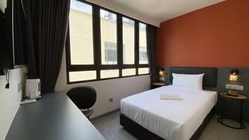 Una habitación de hotel con cama, escritorio, silla y ventana con cortinas.
