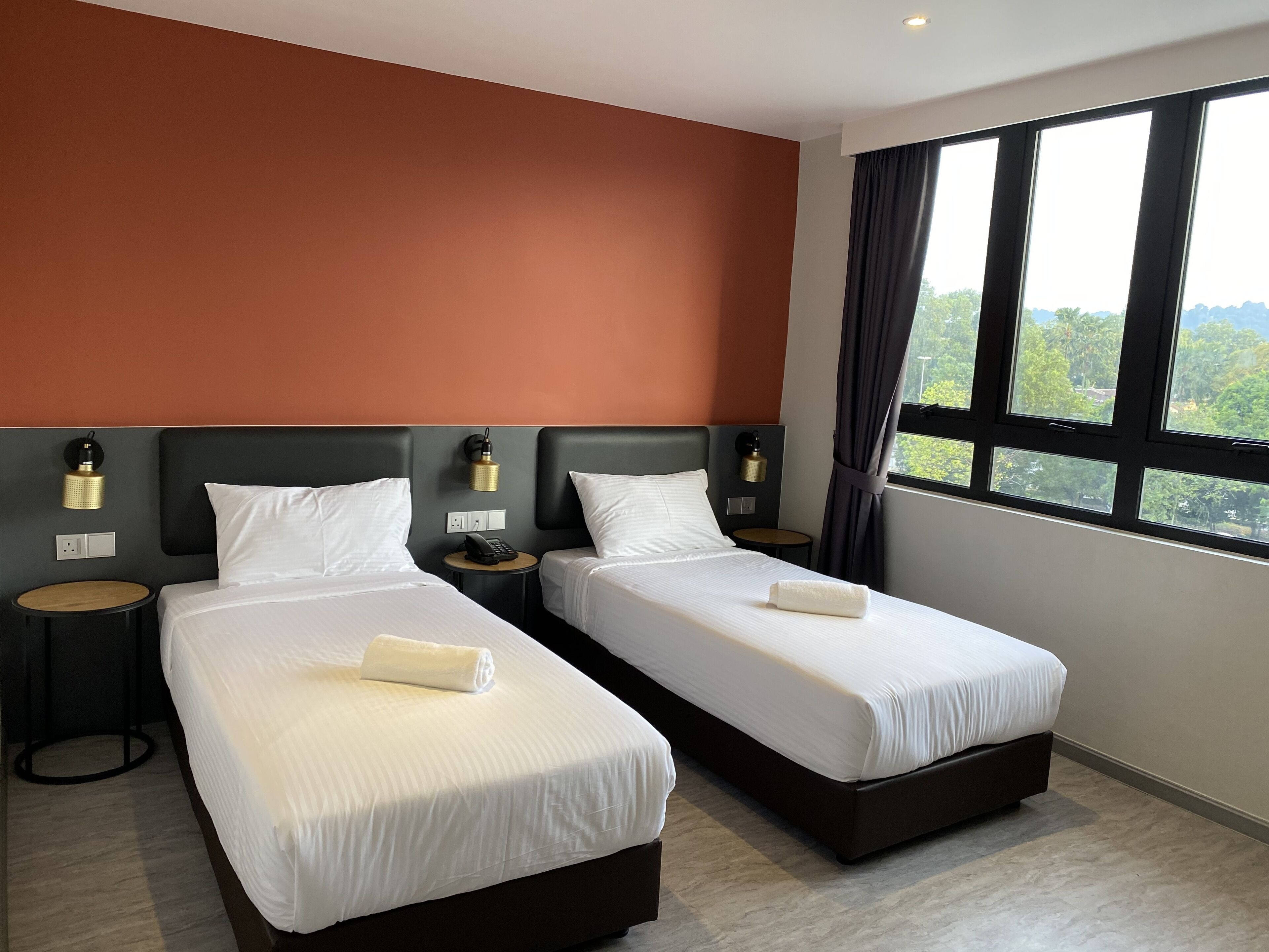 Habitación de hotel con dos camas, una mesa redonda y vistas a zonas verdes a través de amplios ventanales.
