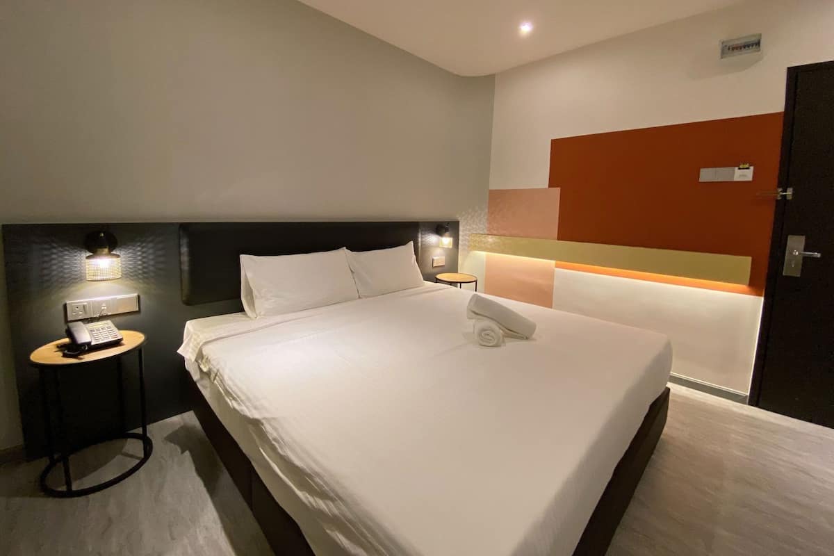 Una habitación de hotel con una cama bien hecha, lámparas de noche, un teléfono y una mesita.