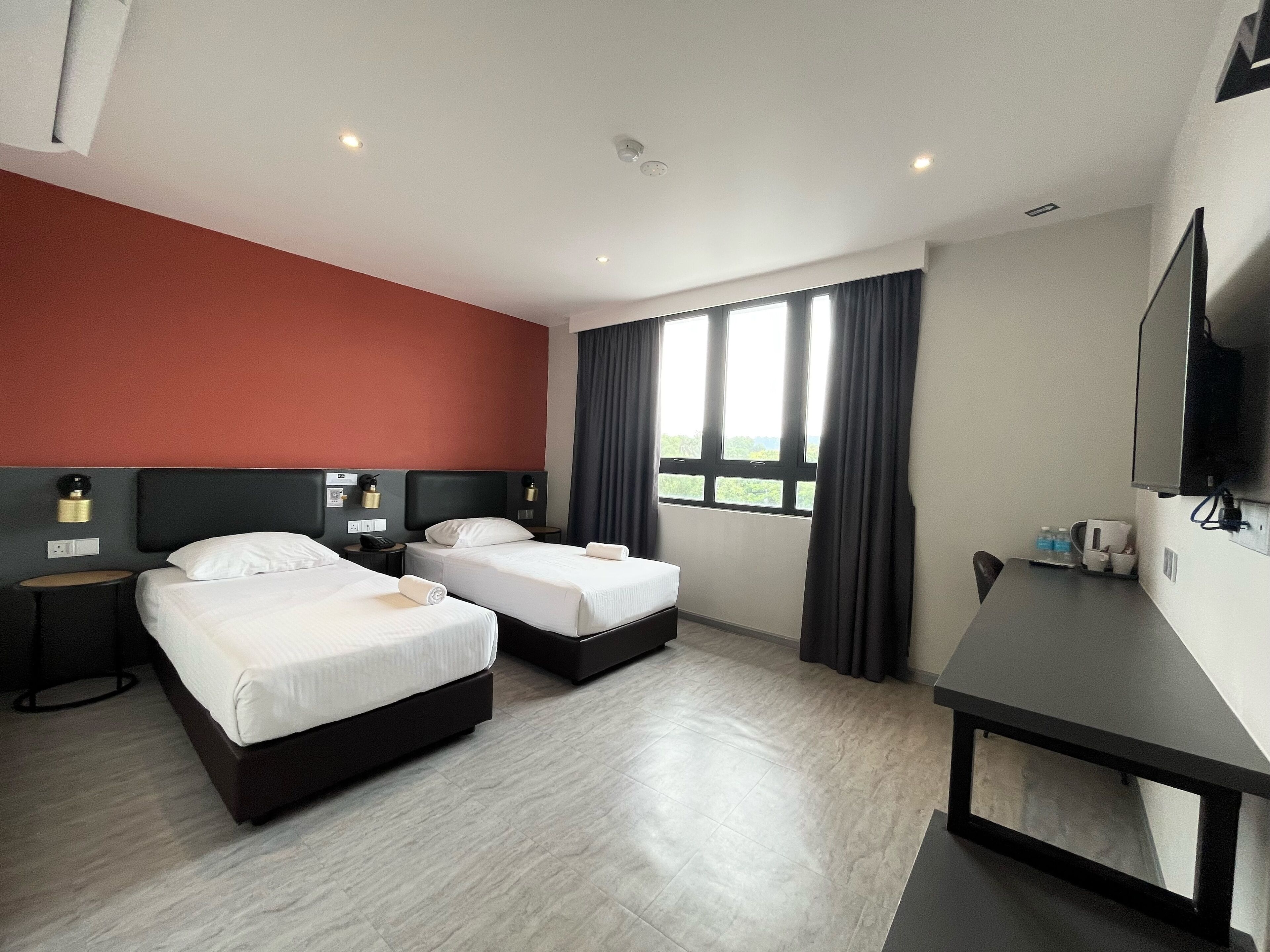 Quarto de hotel com duas camas, uma escrivaninha, televisão e janela com cortinas.