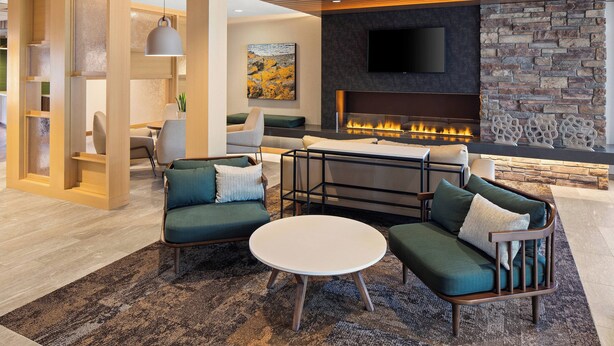 A modern living room with a fireplace, green sofas, a round coffee table, and a flat-screen TV mounted on the wall. - Fairfield Inn & Suites by Marriott Duluth (Duluth)