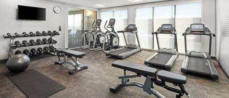 Une salle de sport équipée de tapis de course, de vélos elliptiques, d’haltères et d’un vélo d’appartement.